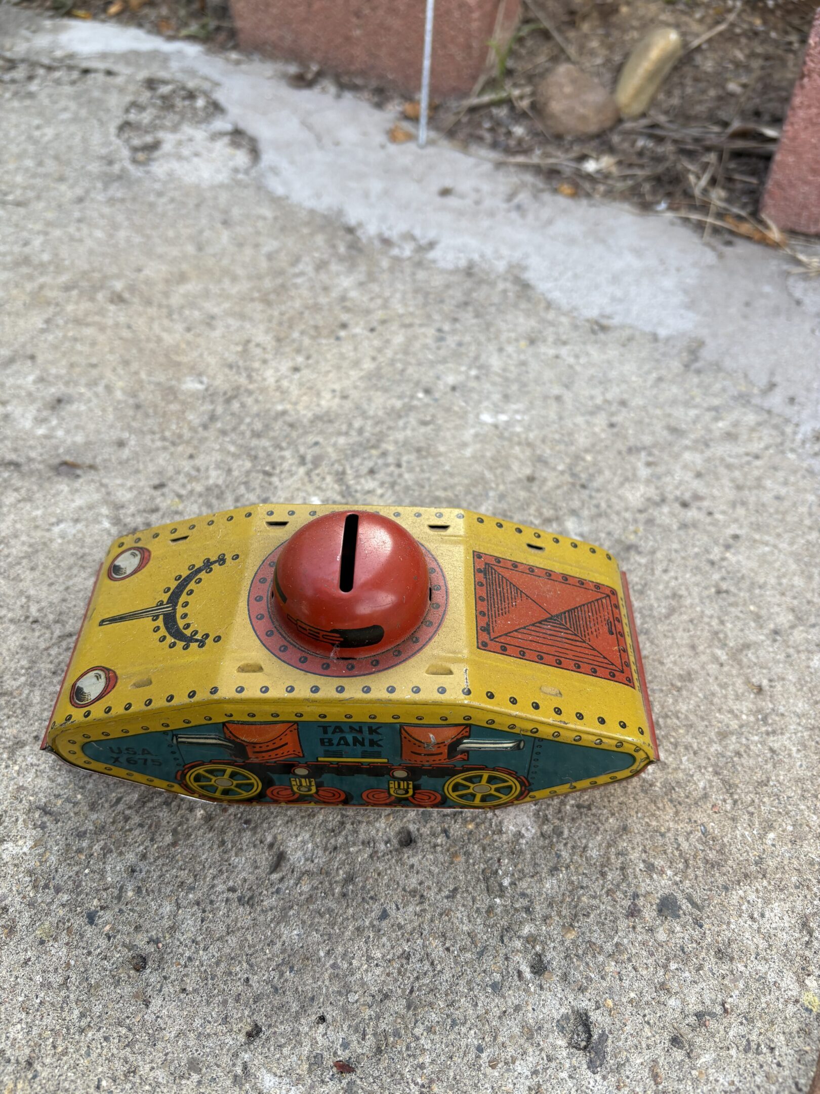 Vintage tin toy tank with bright colors on concrete.