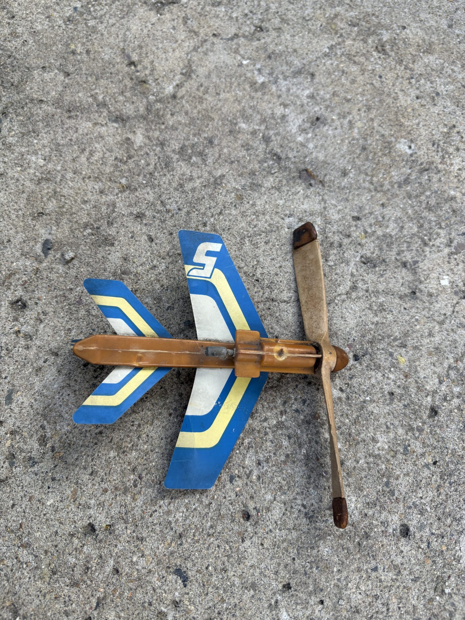 A handmade wooden toy airplane with blue and white wings on concrete.