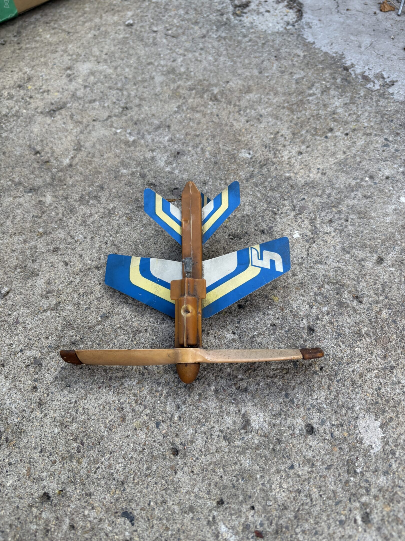 Handcrafted wooden toy airplane with blue and white wings on concrete.
