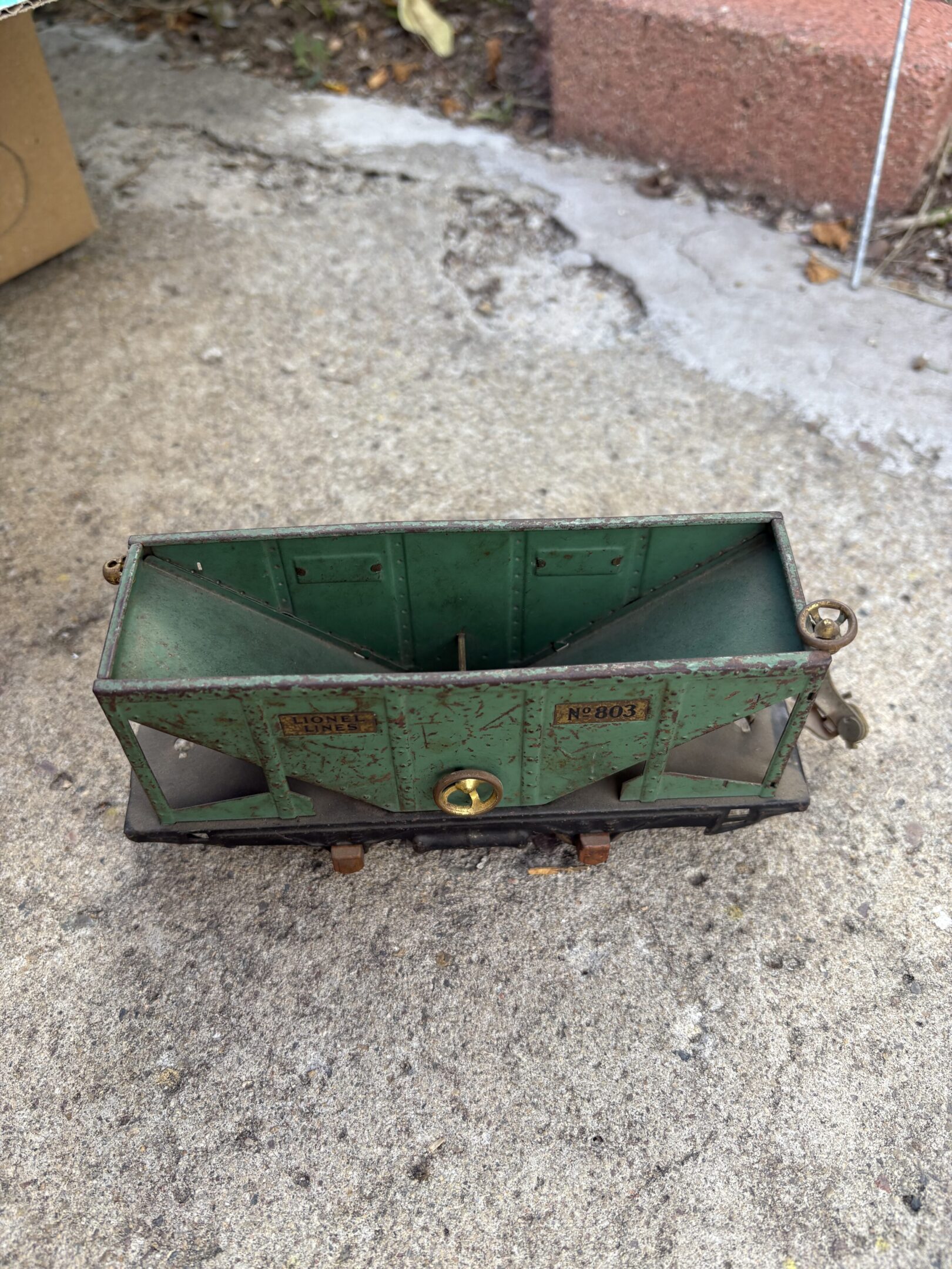 Old green metal container with rust on a concrete surface.