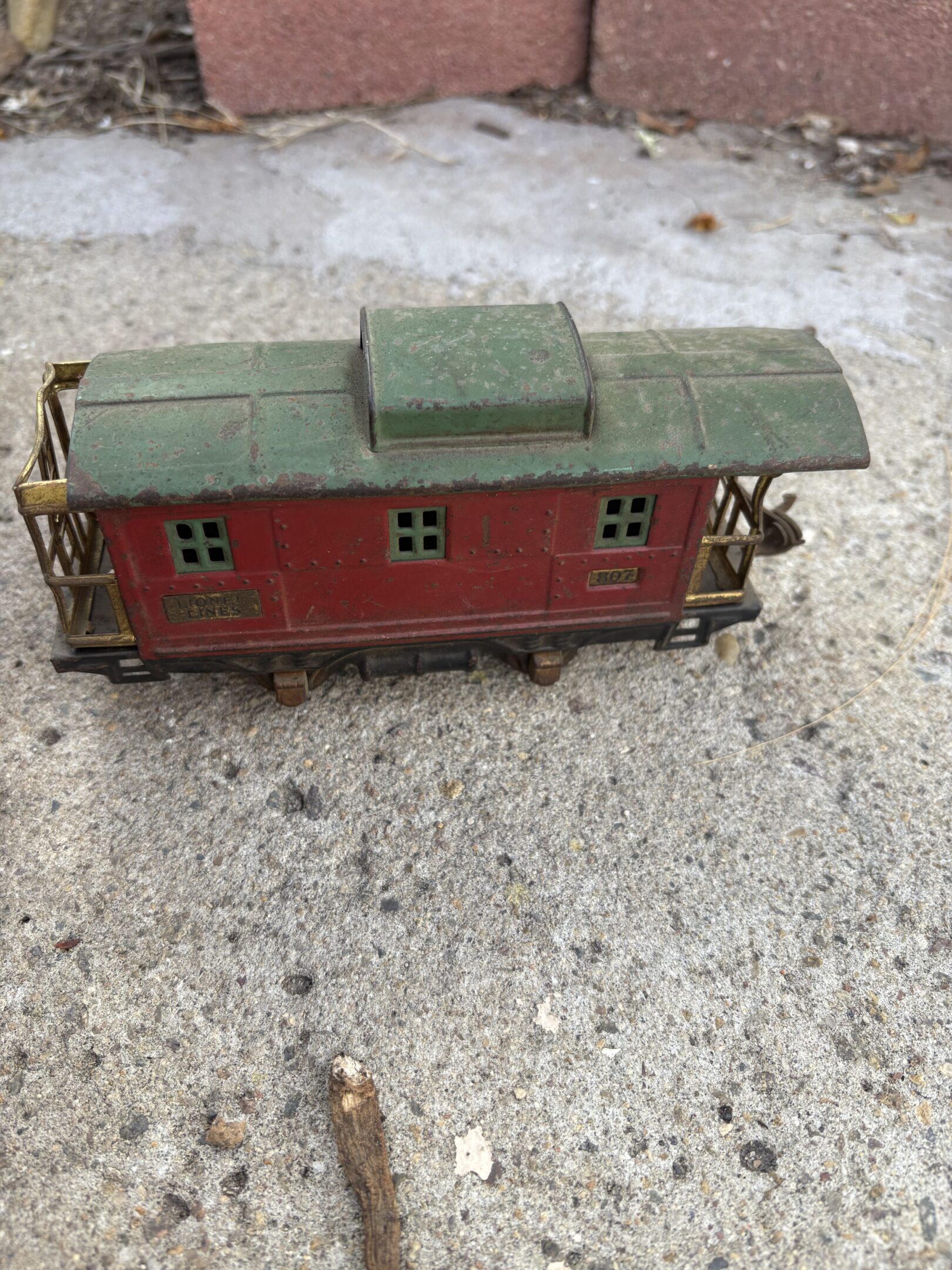 Vintage red caboose model train car with green roof on concrete.