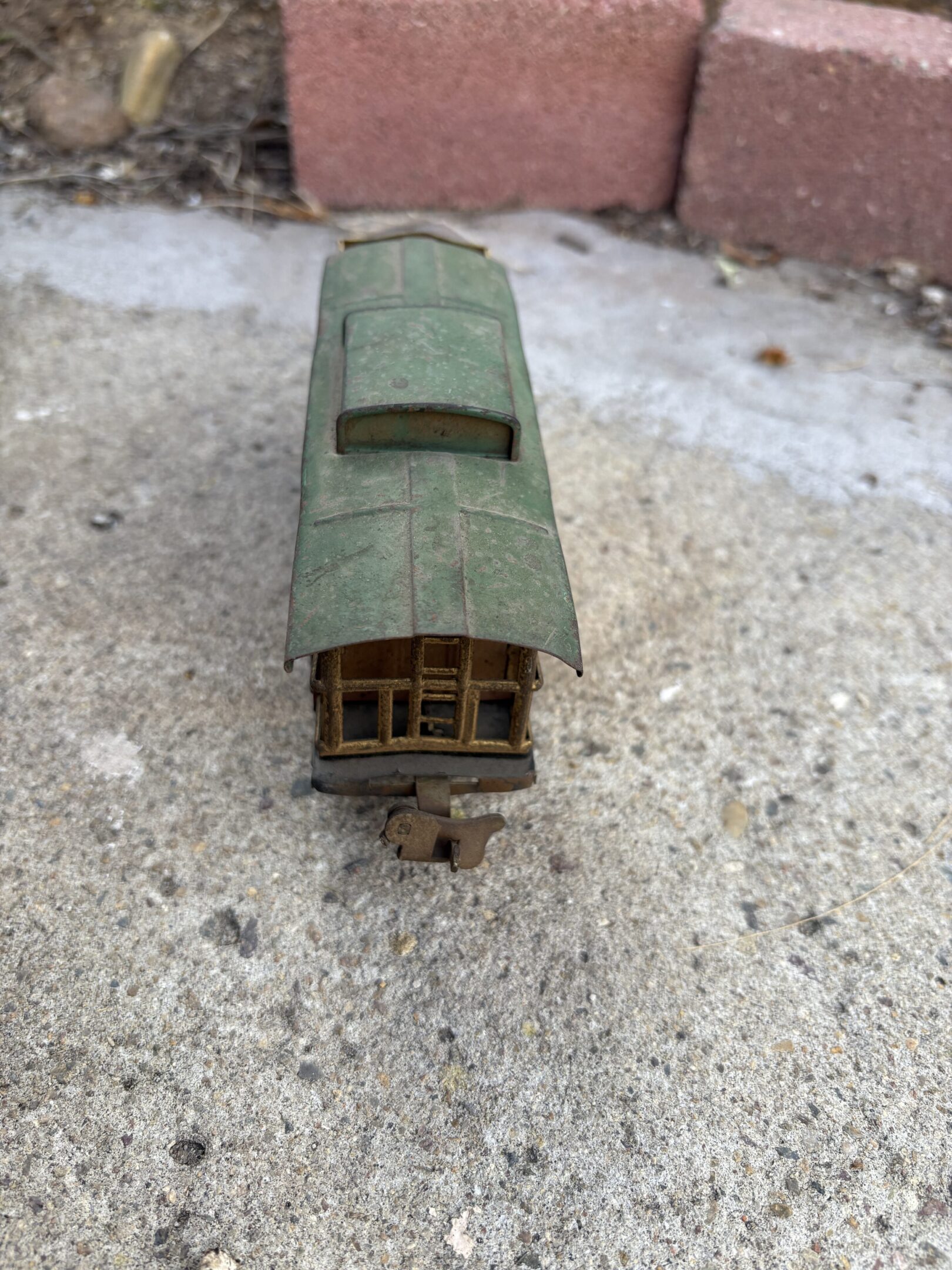 A vintage green toy train carriage on a rough concrete surface.