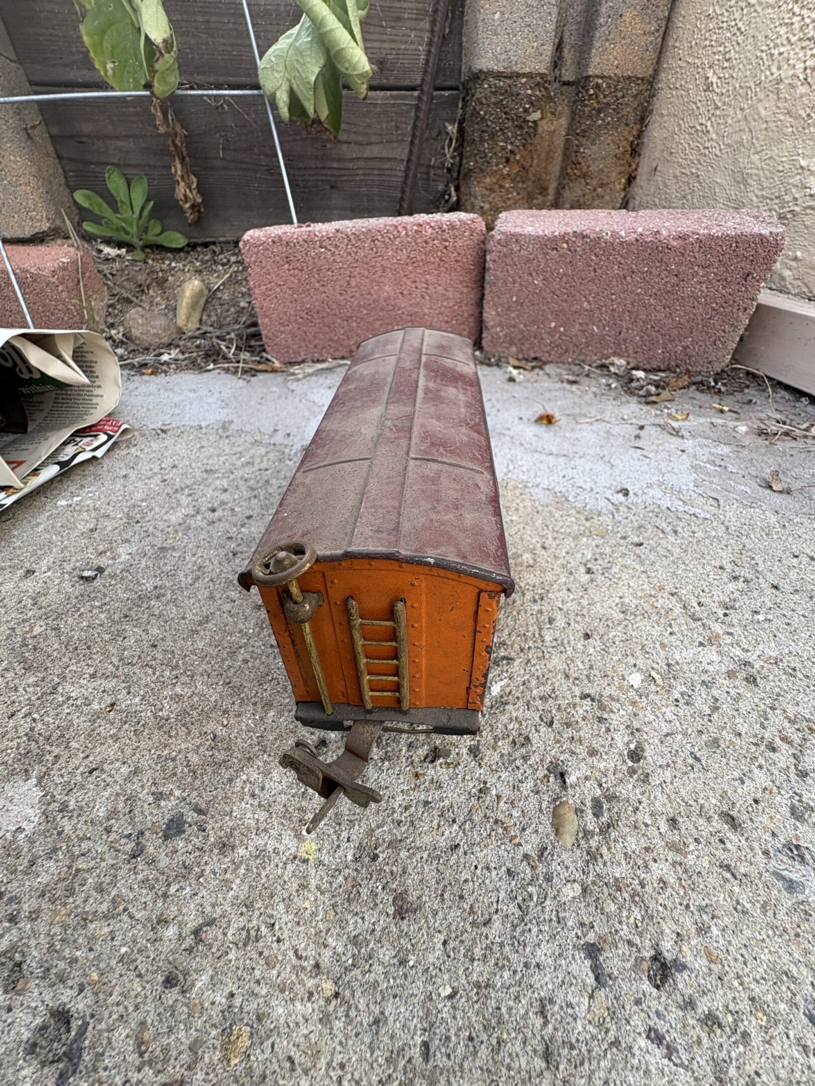 Rusty model train car on a concrete surface outdoors.