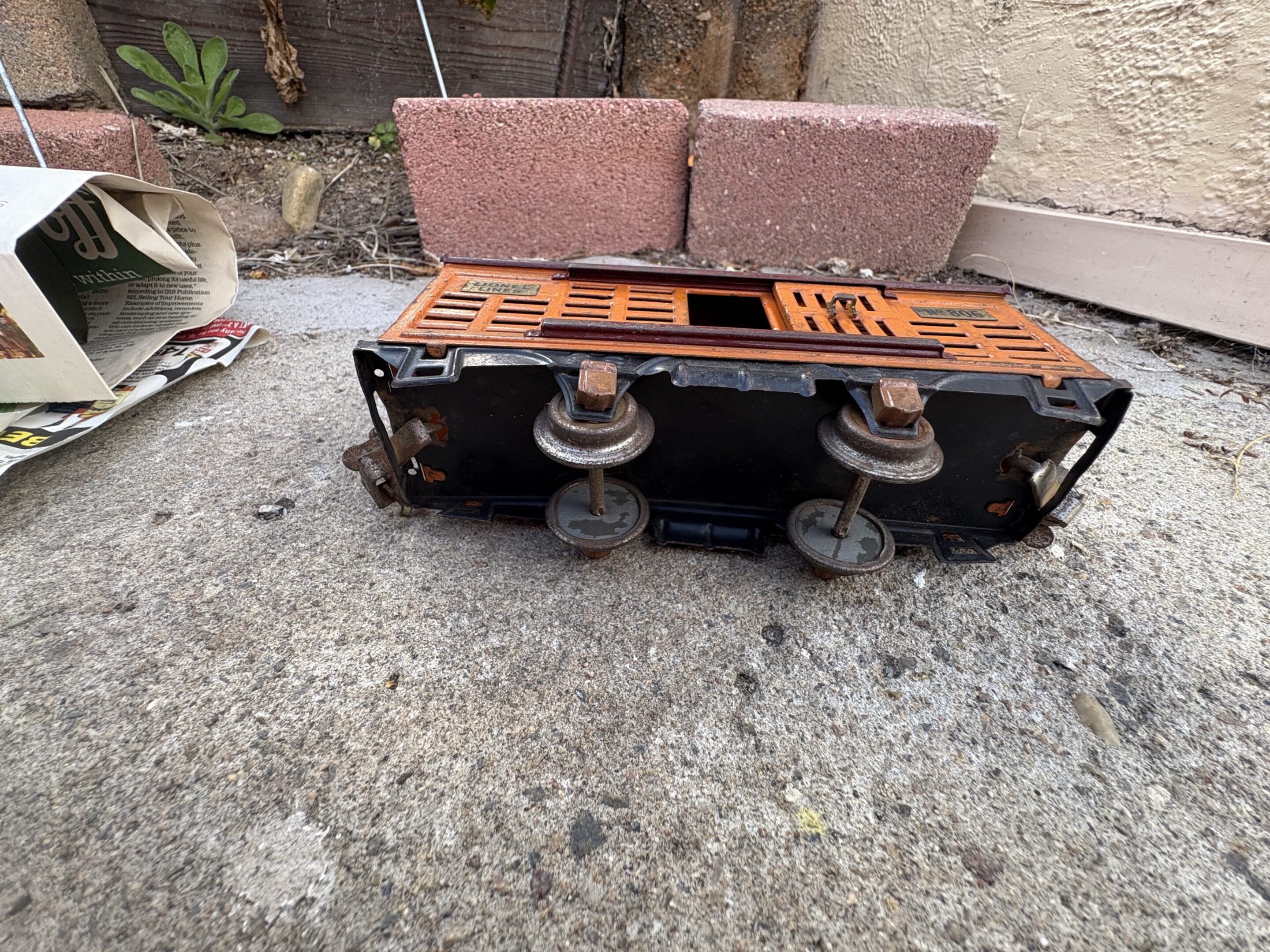 A rusty car suspension part on concrete ground with bricks in the background.