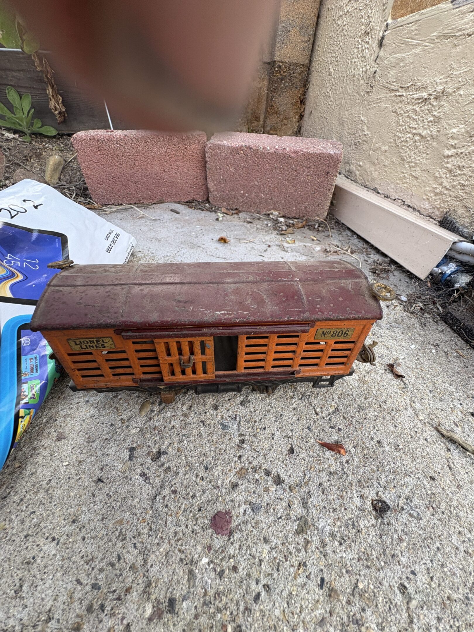 A vintage wooden toy train car on a concrete surface with bricks nearby.