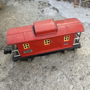 Vintage red toy train caboose with yellow windows on tracks.