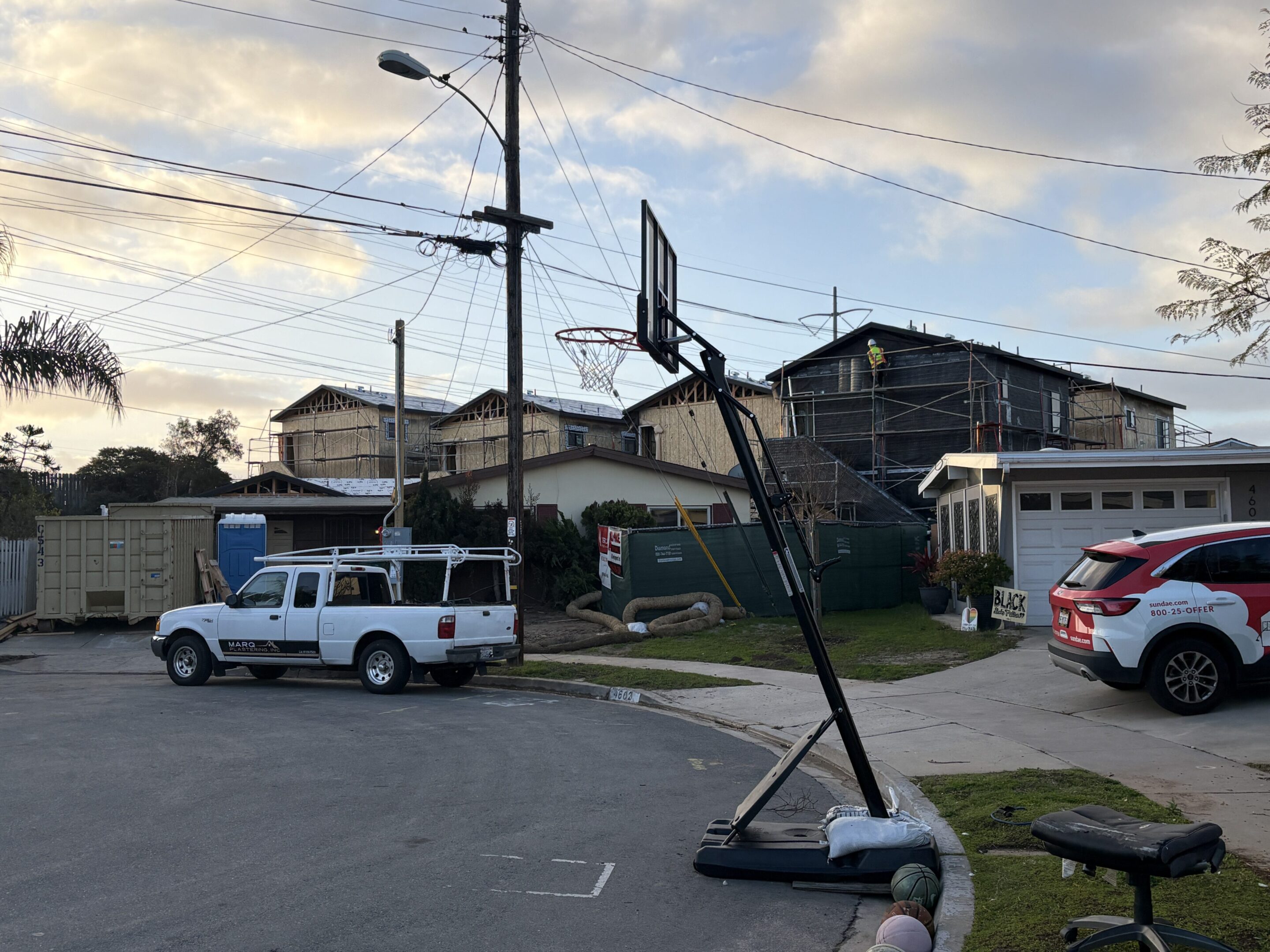A portable basketball hoop leaning over in a parking lot at sunset.