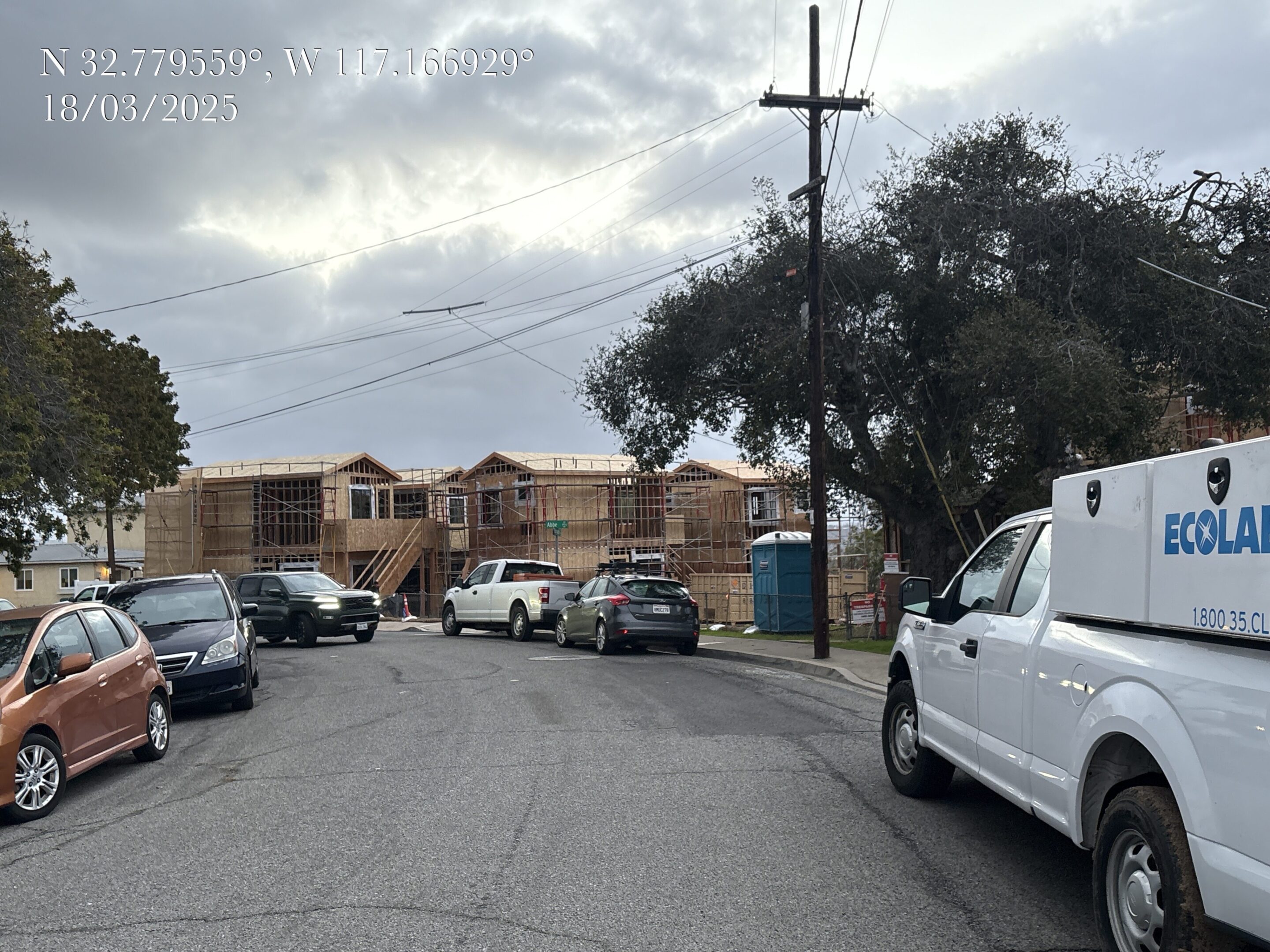 Construction of new houses on a residential street with cars parked nearby.