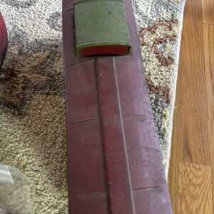 A green foam block attached to a thin metal rod on a carpeted floor.