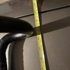 Measuring a black pipe with a yellow tape measure against a brown surface.