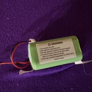 A rechargeable Ni-MH battery pack with warning labels on a purple background.