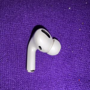 A single white wireless earbud on a purple textured surface.