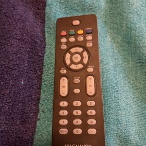 A black remote control with multiple buttons on a fabric surface.