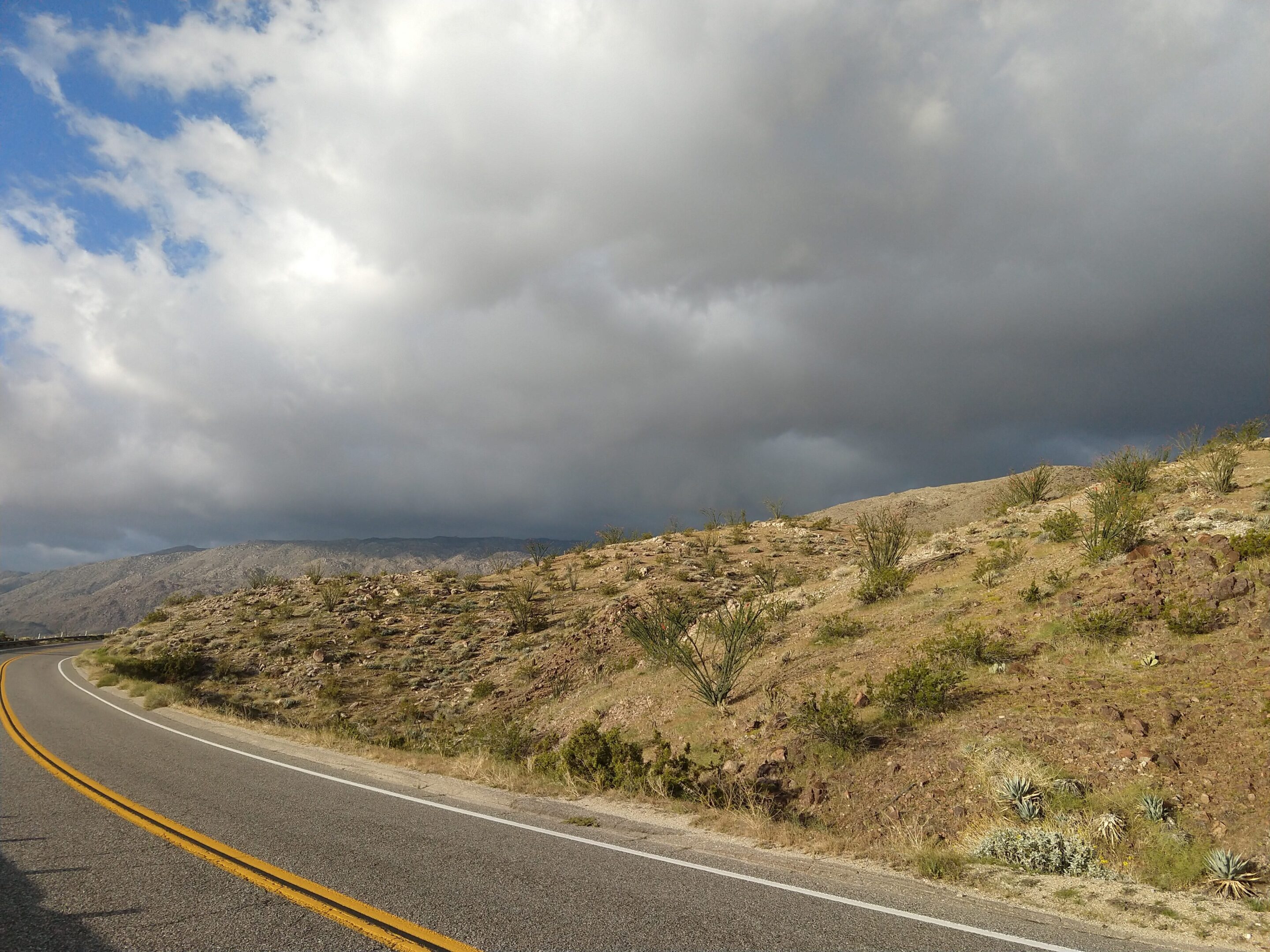 Road winding through a dry, hilly landscape under a cloudy sky.