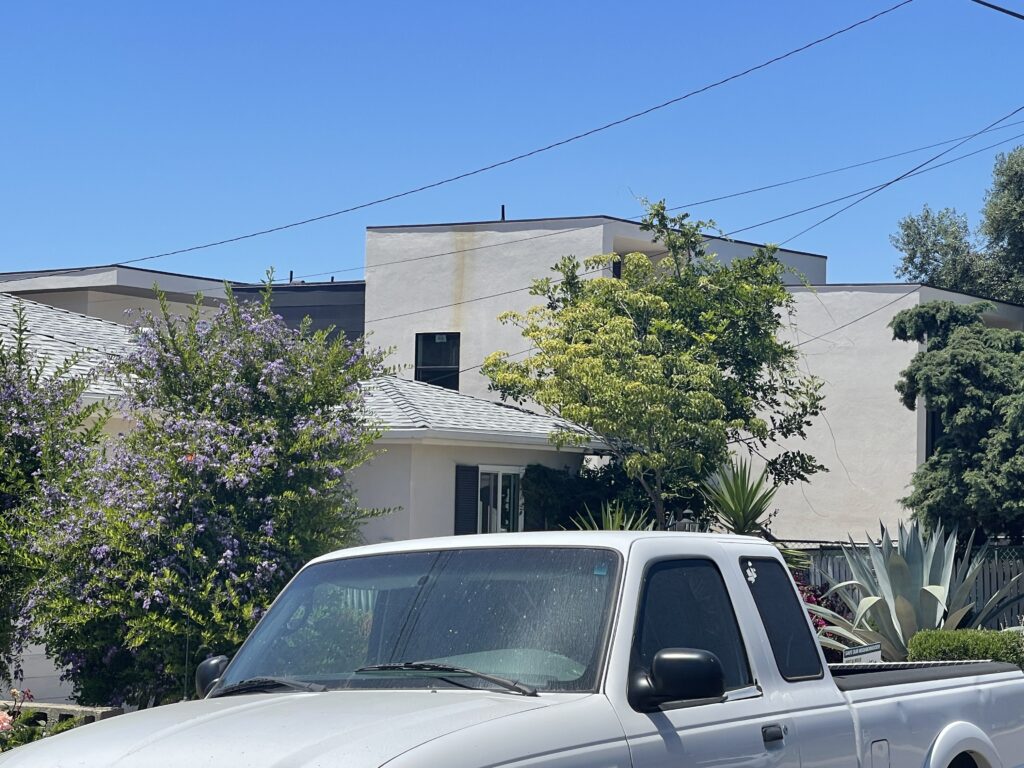 A white pickup truck parked in front of a concrete building with trees.